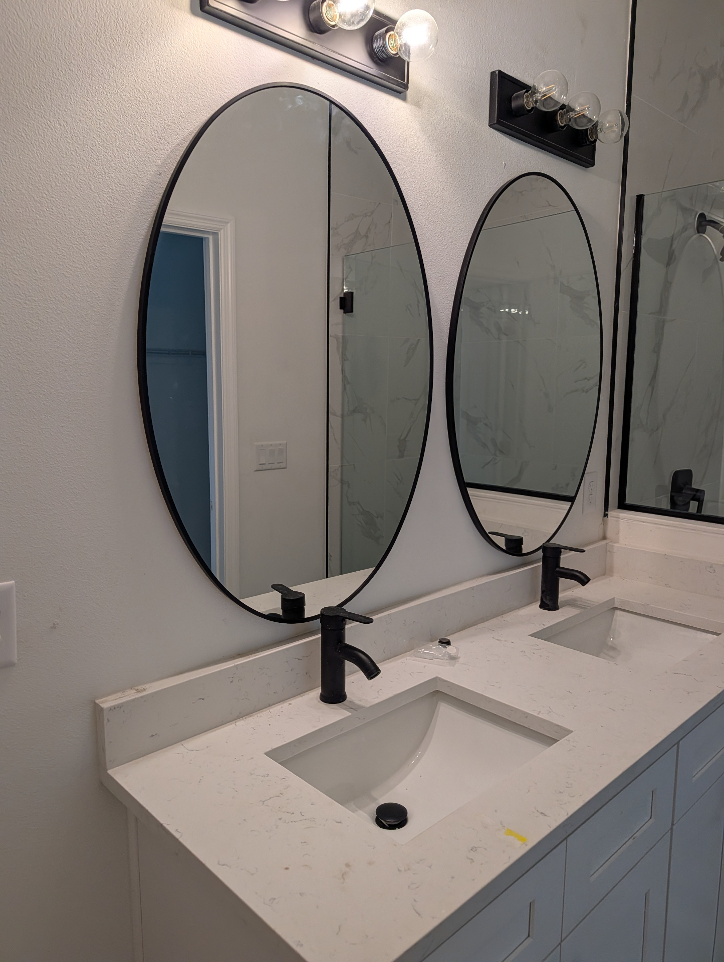 Finished Tampa bathroom with white double vanity, quartz top and oval black-framed mirrors